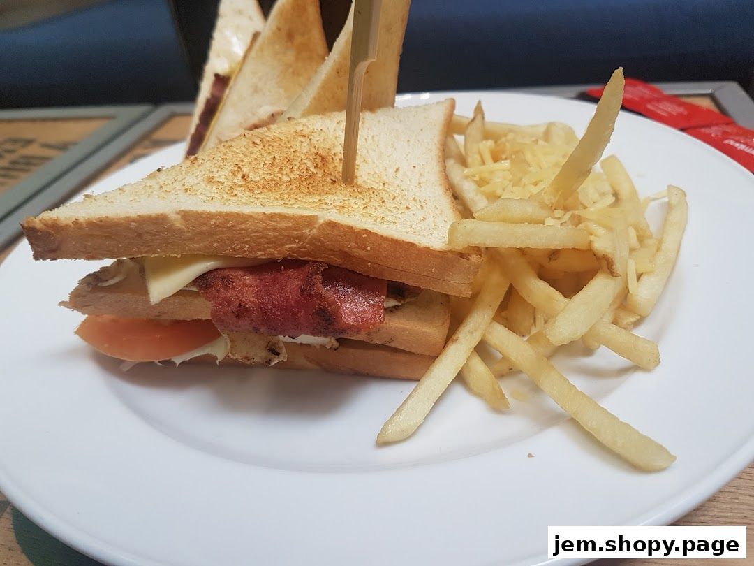 A club sandwich with fries and shredded cheese on a white plate.