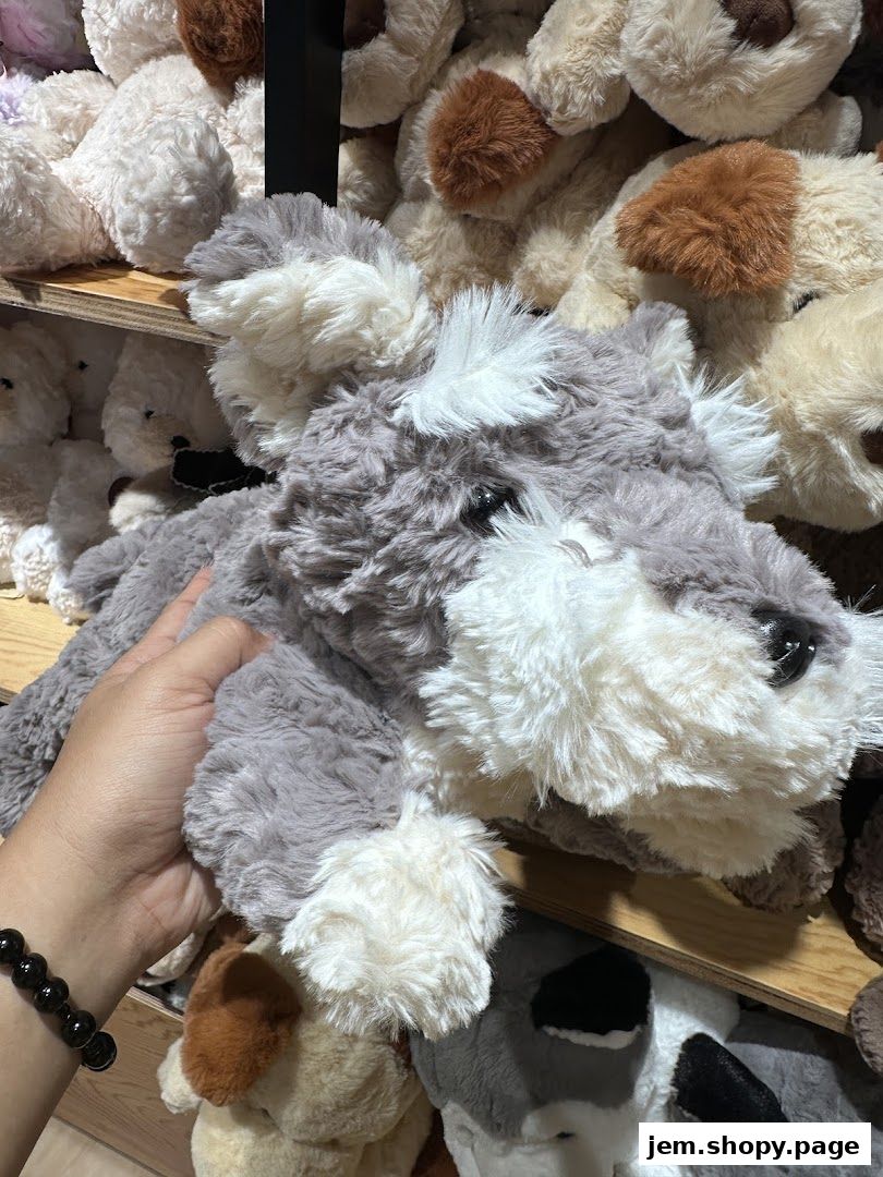 A hand holds a fluffy grey and white stuffed dog in a shop filled with plush toys.