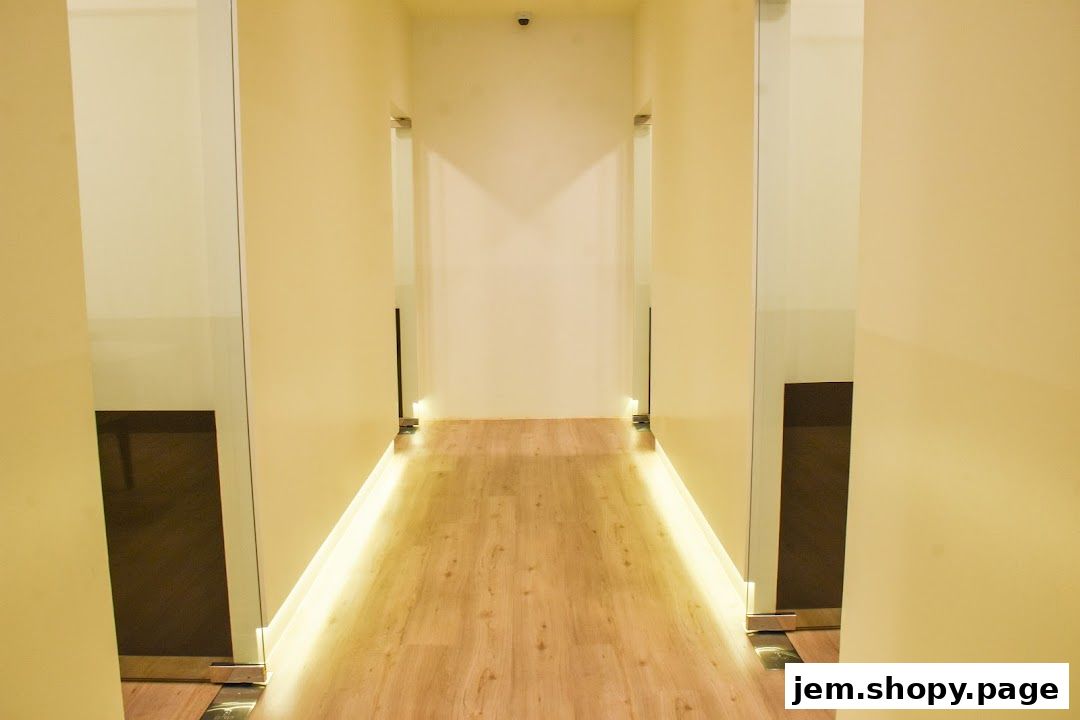 A modern hallway with wooden floors and illuminated walls, leading to rooms with glass doors.