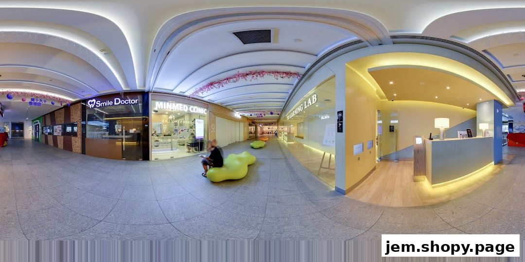 A wide shot of a modern shopping mall corridor with various shops and seating areas.