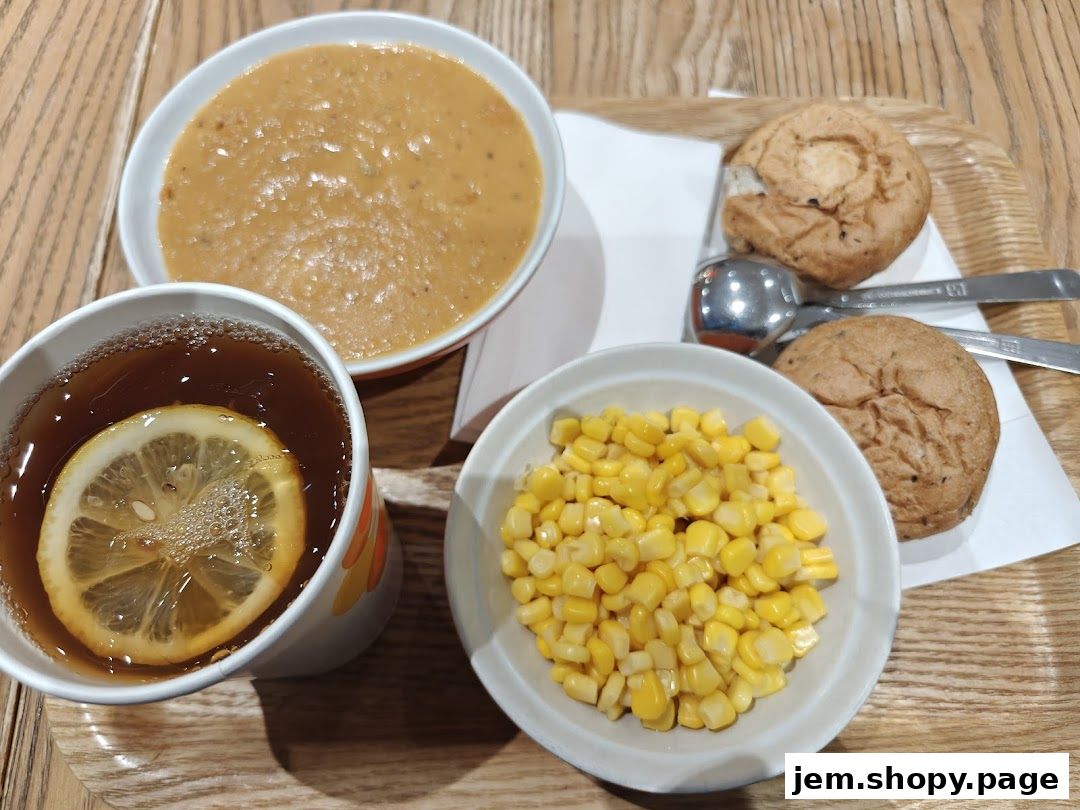 A meal set with soup, corn, bread rolls, and a lemon tea.