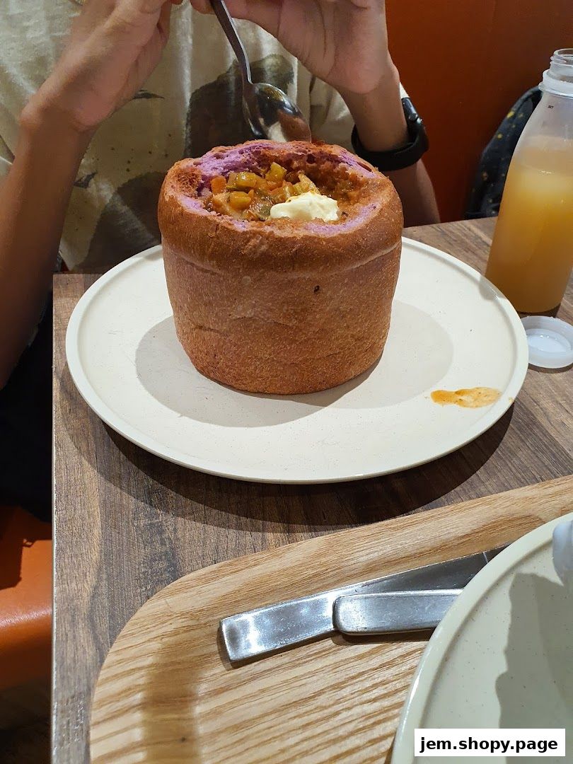A person is eating a hearty soup served in a hollowed-out bread bowl.