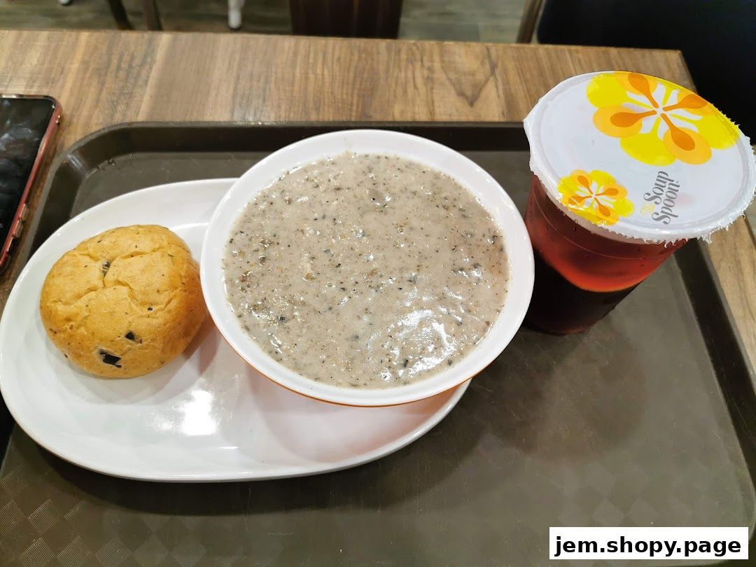 A bowl of creamy mushroom soup with a side bun and a drink from The Soup Spoon.