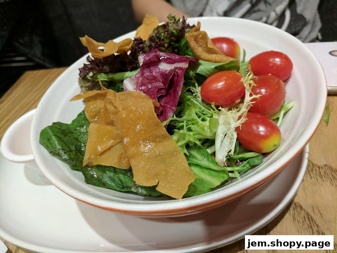 A fresh salad with cherry tomatoes and crispy wonton strips in a white bowl.