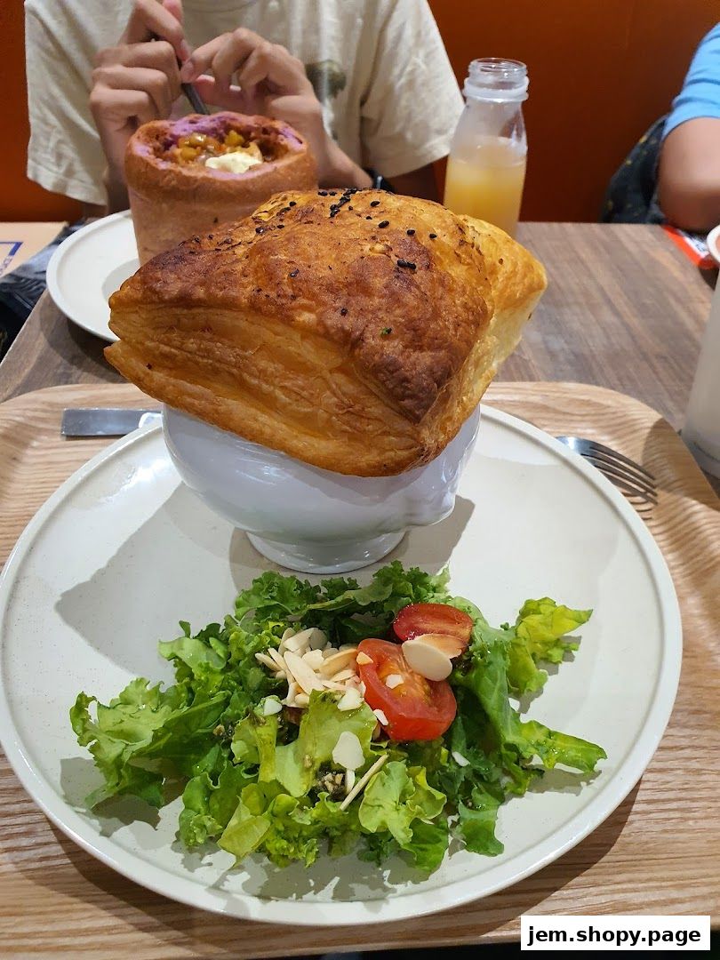 A close-up of a flaky pastry-topped soup served with a side salad.