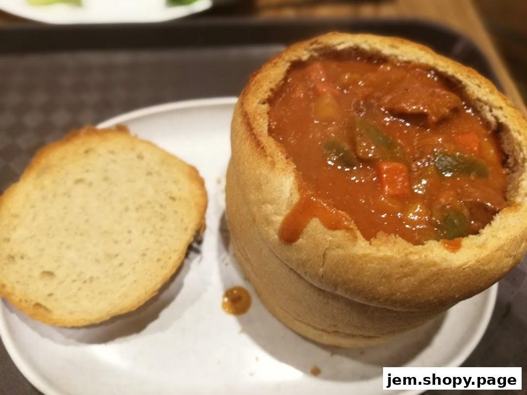 A hearty stew served in a hollowed-out bread bowl with a side of bread.