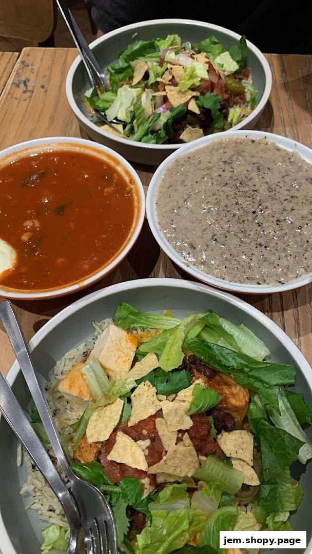 Three bowls of food, including soup, salad, and a rice bowl, are arranged on a wooden table.