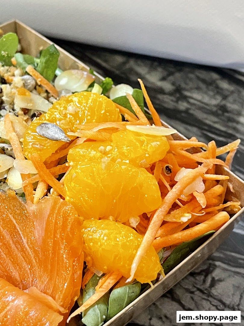 A close-up of a healthy salad with salmon, oranges, and shredded carrots.