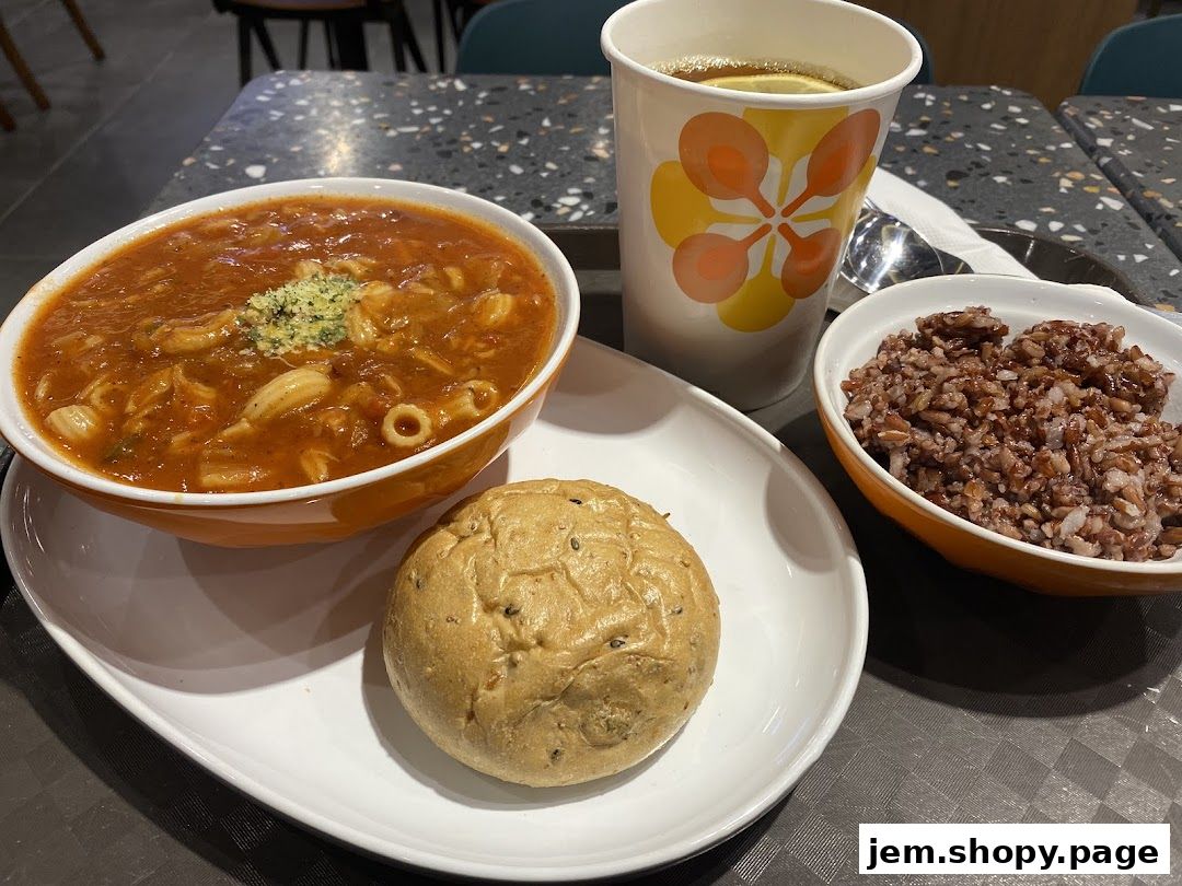 A hearty bowl of tomato pasta soup with a side of brown rice and a bread roll.