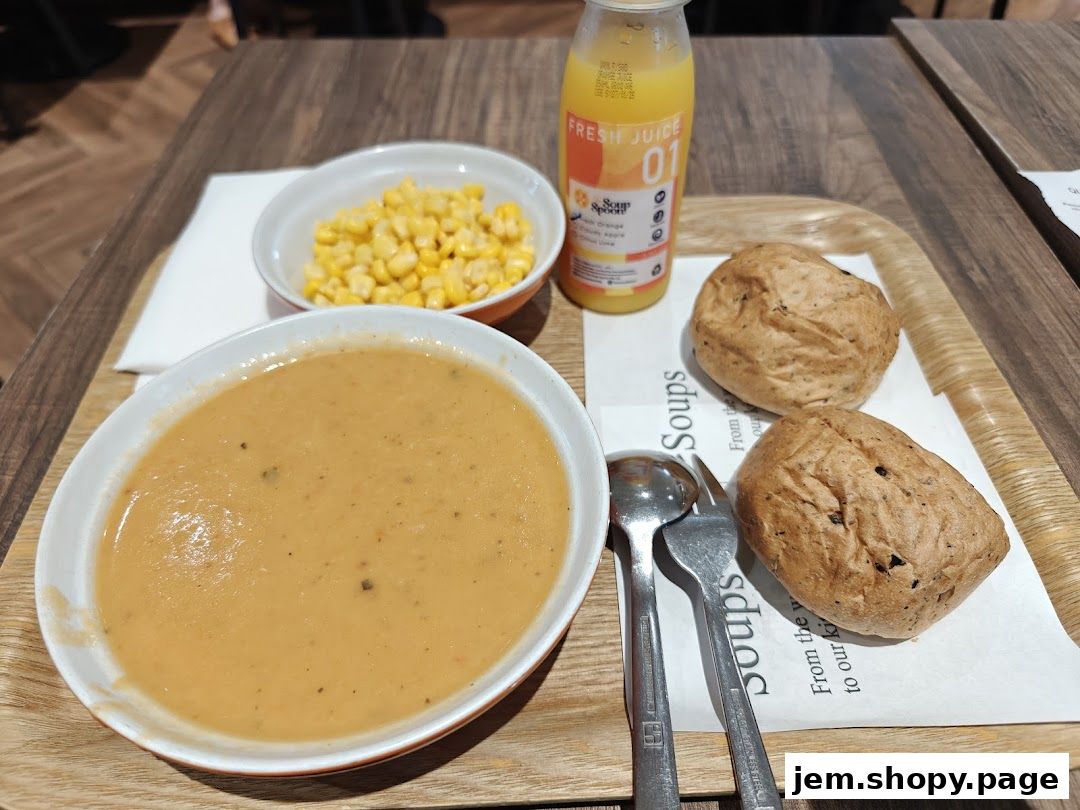 A bowl of soup, corn, bread rolls, and a bottle of juice on a tray.