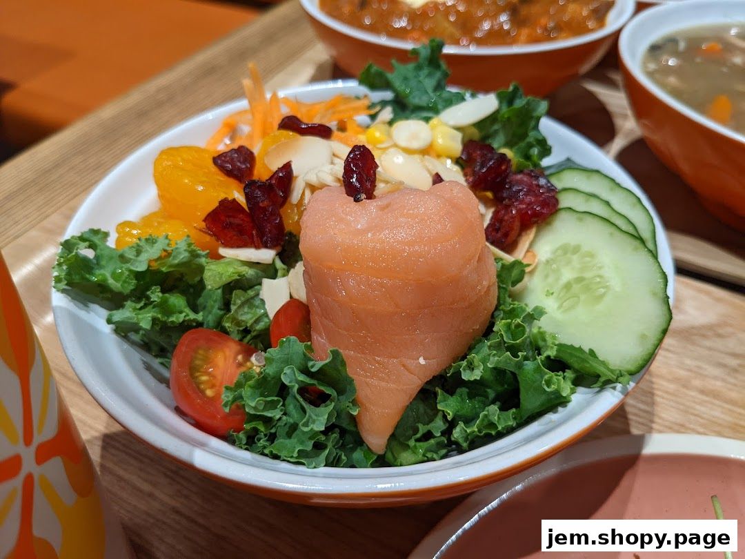 A close-up of a salmon salad with various fresh ingredients and a side of soup.