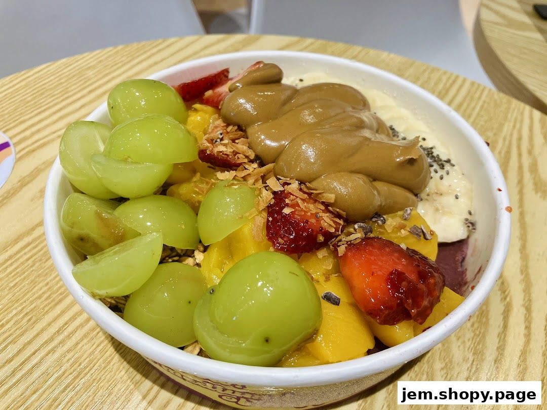 A close-up of a refreshing açaí bowl topped with grapes, strawberries, mango, banana, and peanut butter.