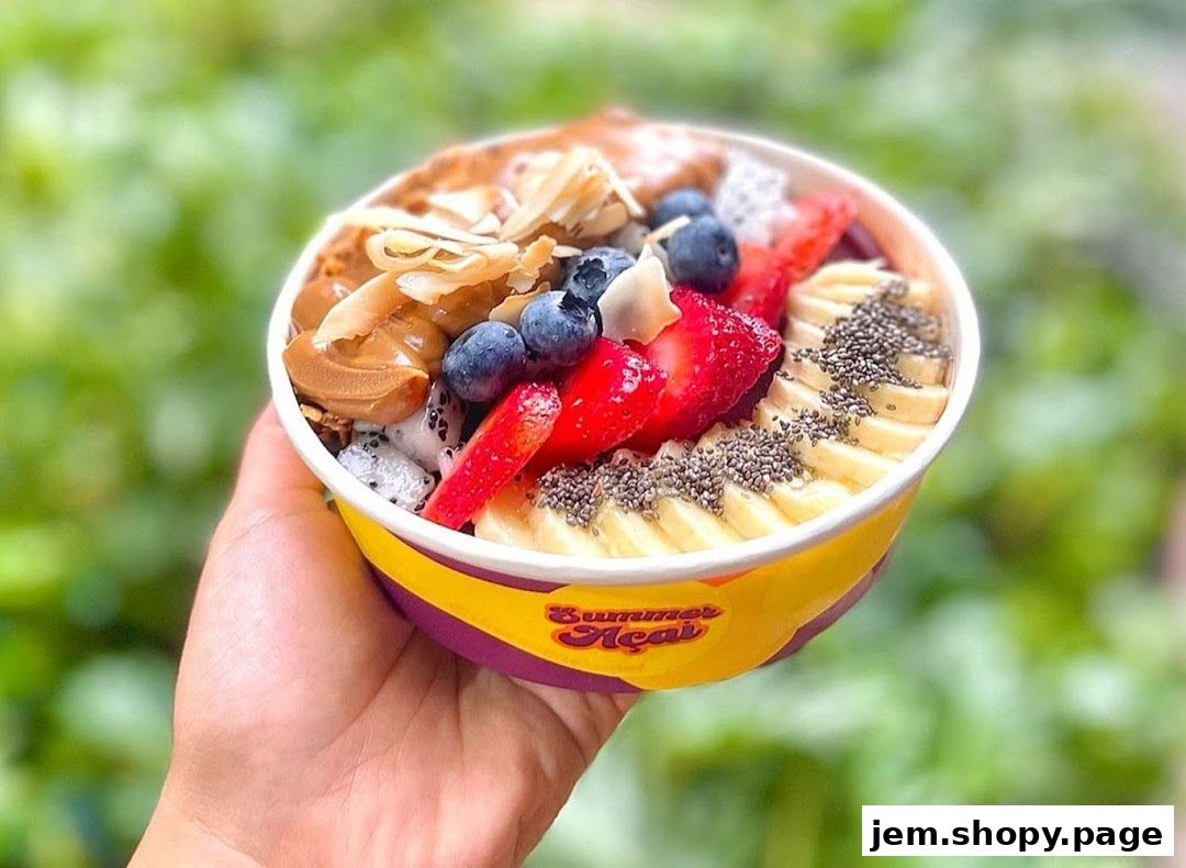 A hand holds a colorful açaí bowl filled with fruits and toppings.