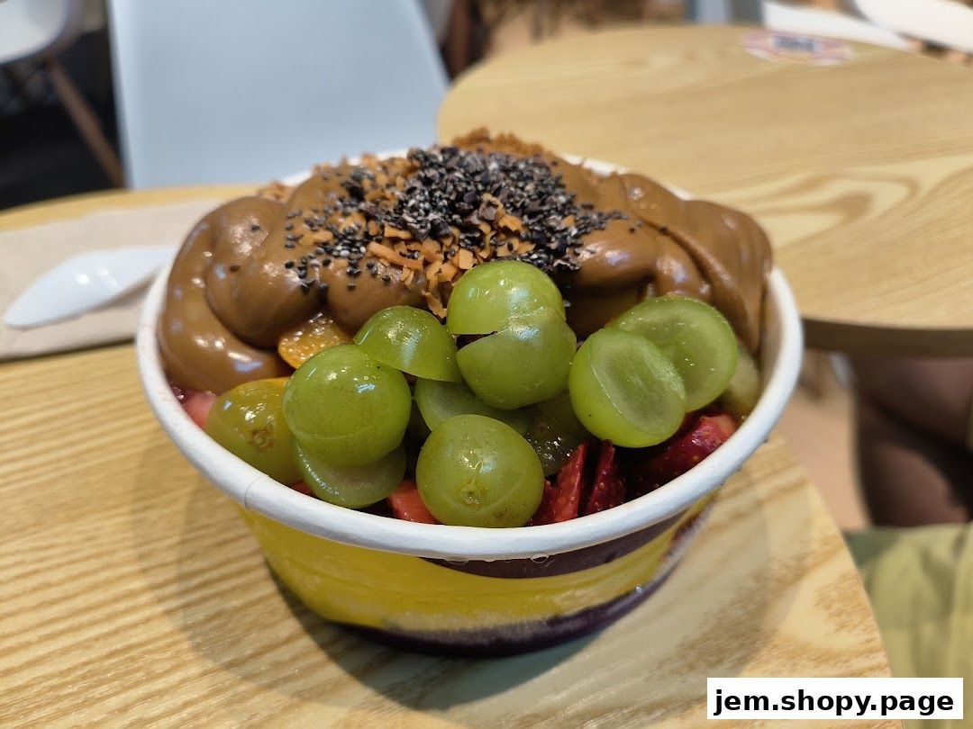 A close-up of a delicious açaí bowl topped with grapes, strawberries, and a creamy sauce.