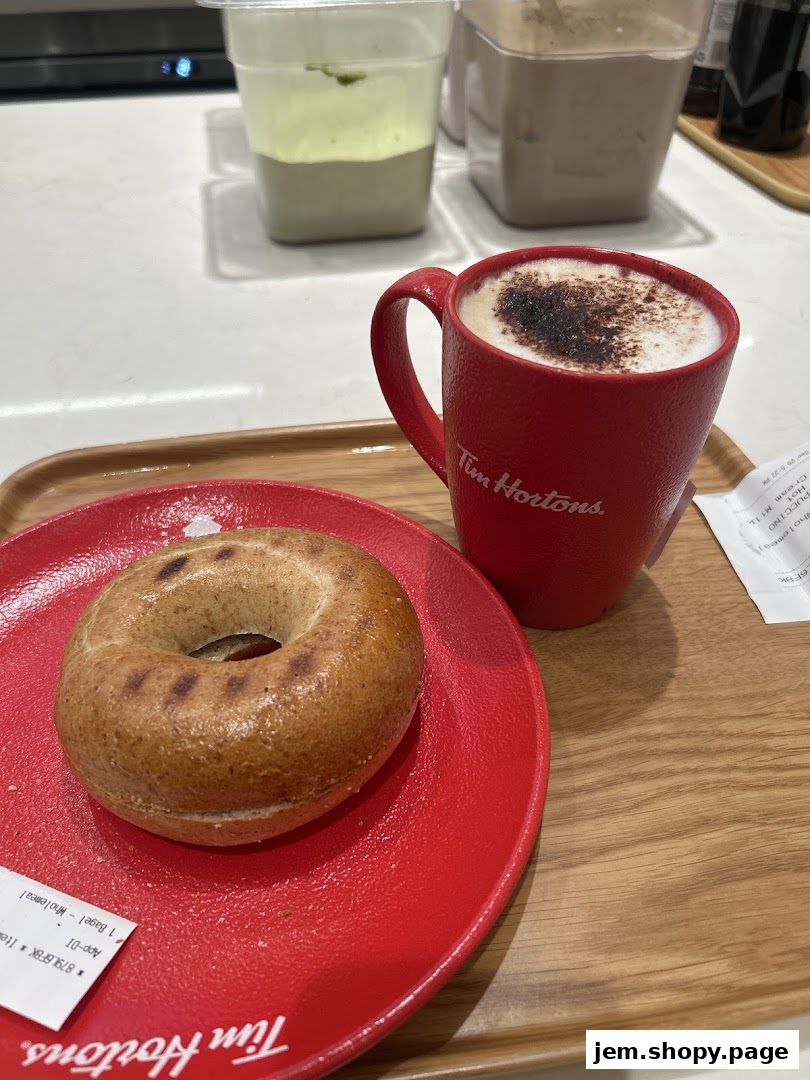 A red mug of cappuccino and a wholemeal bagel on a tray.