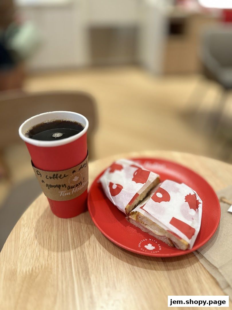 A red cup of coffee and a sandwich on a red plate on a wooden table.