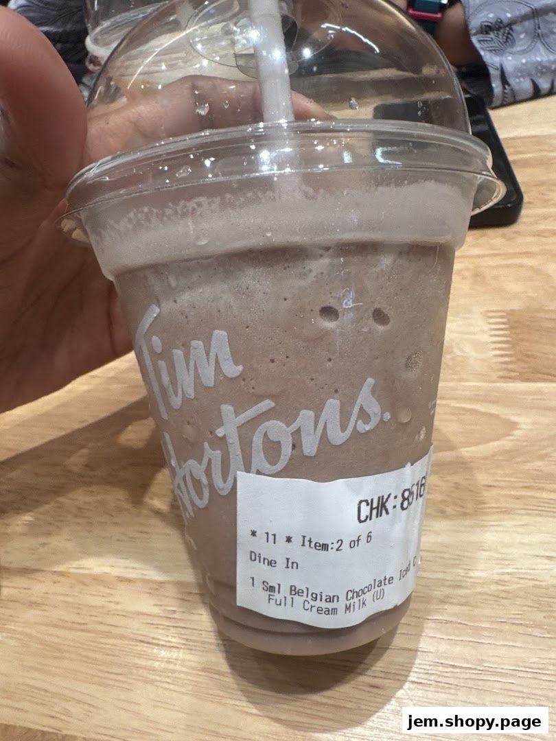 A hand holds a small Tim Hortons Belgian Chocolate Iced Capp with a receipt sticker.