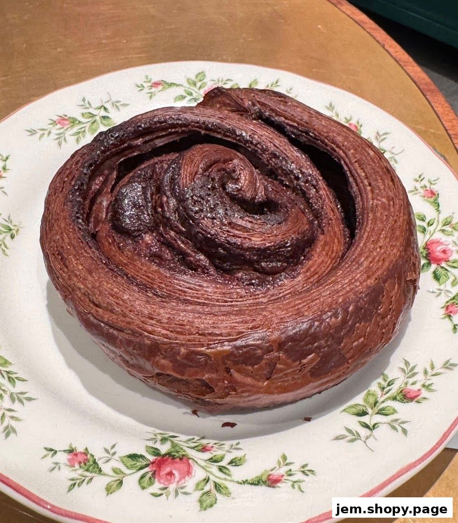 A close-up of a chocolate swirl pastry on a floral-patterned plate.