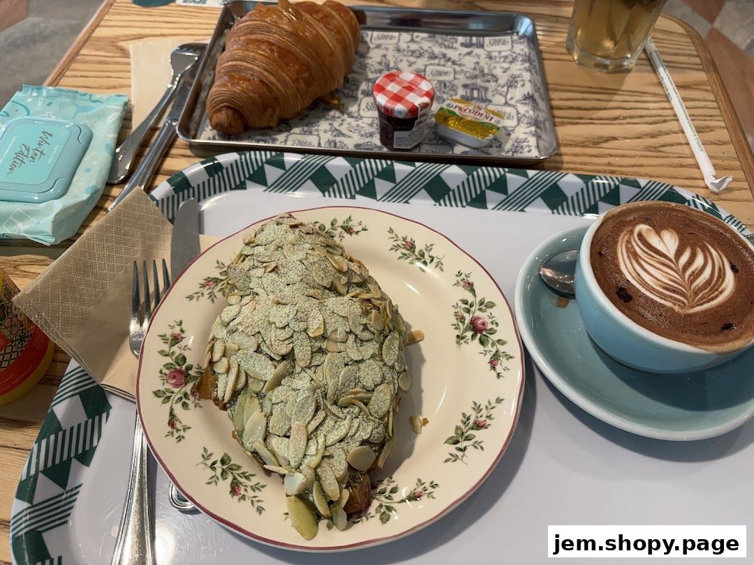 A close-up of a table with two croissants, a coffee, and jam.
