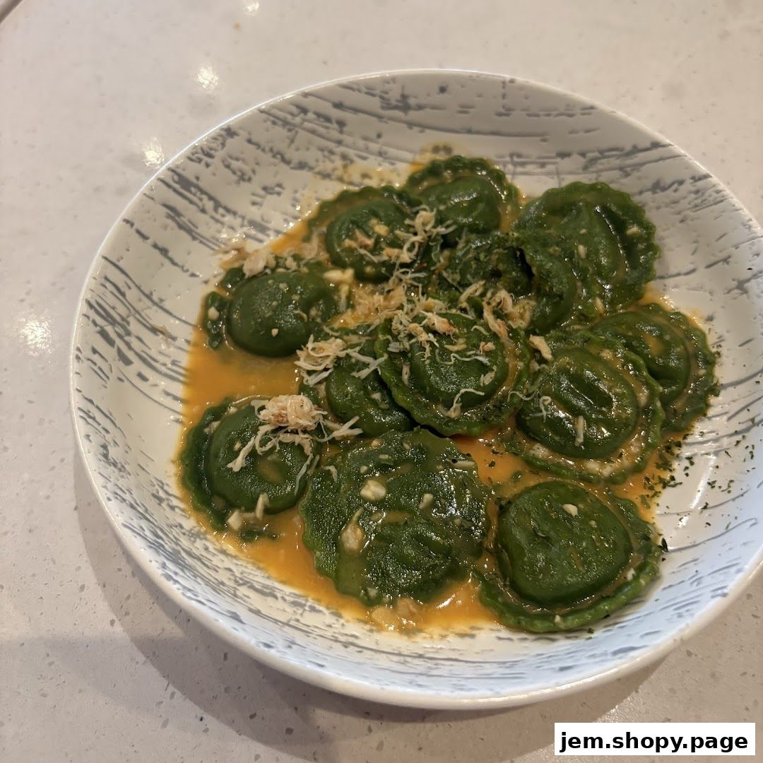 A close-up shot of green ravioli in a creamy sauce, topped with shredded cheese.