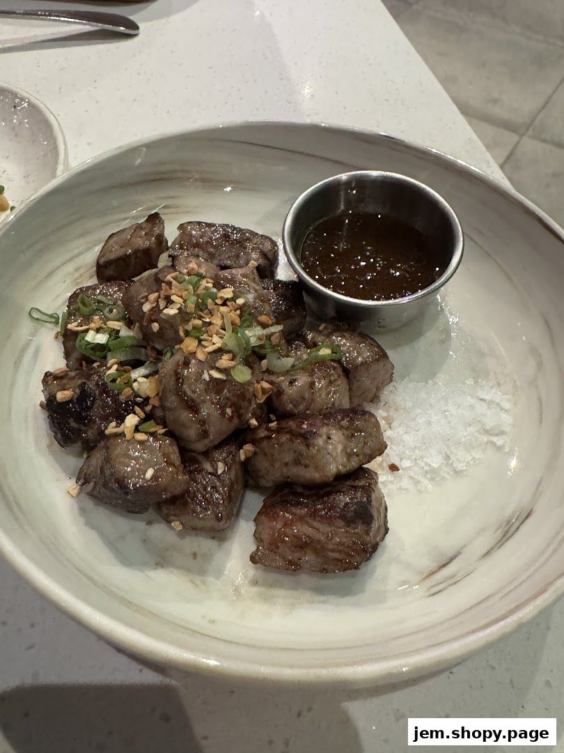 A close-up of a dish featuring bite-sized pieces of grilled meat with a dipping sauce.