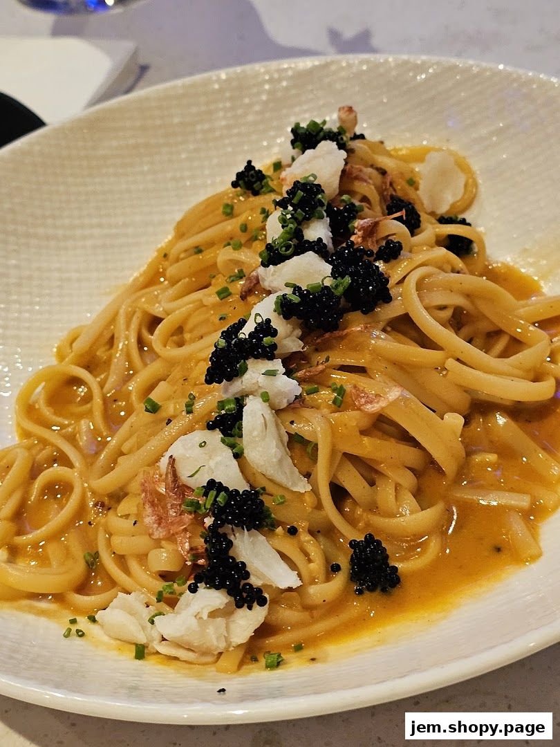 A plate of linguine pasta with a creamy orange sauce, crab meat, and black caviar.