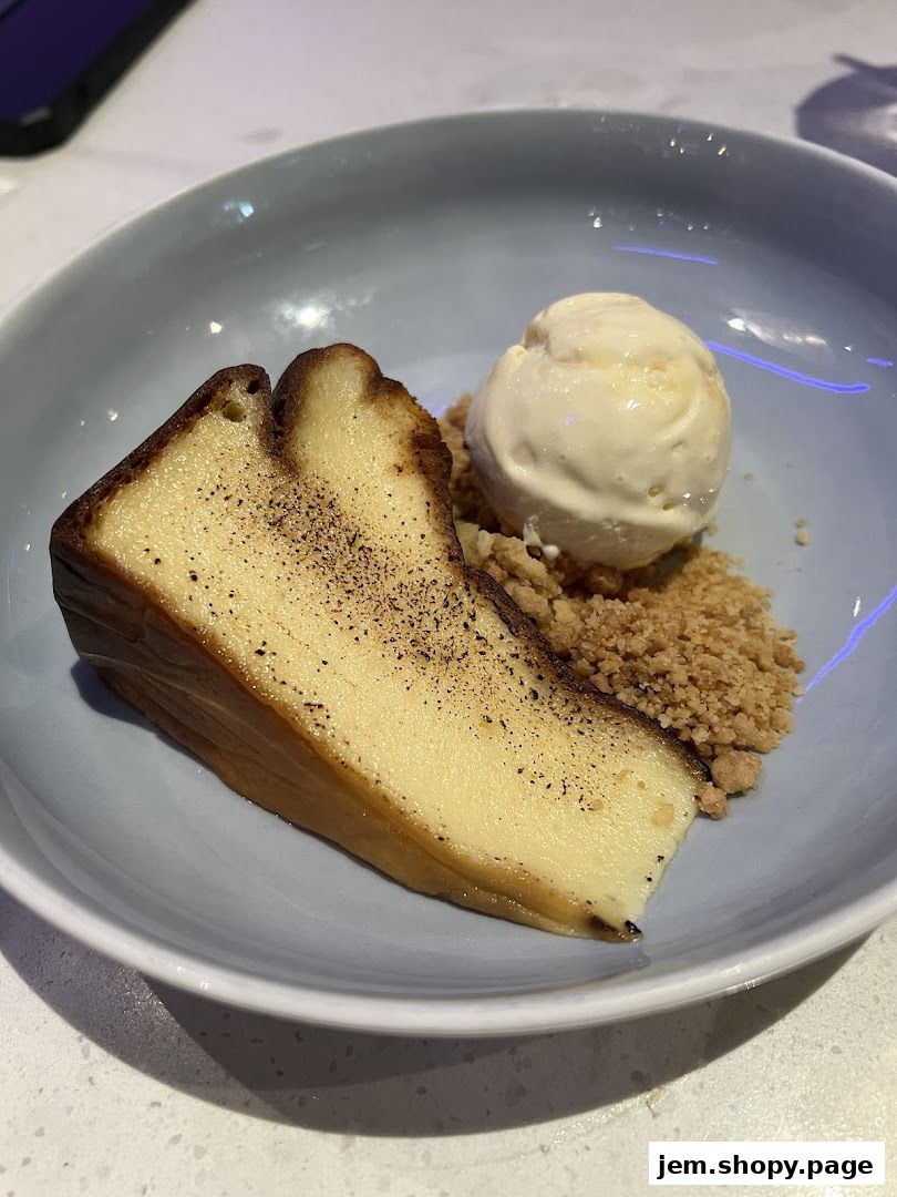 A slice of cheesecake with ice cream and crumble topping served in a light blue bowl.
