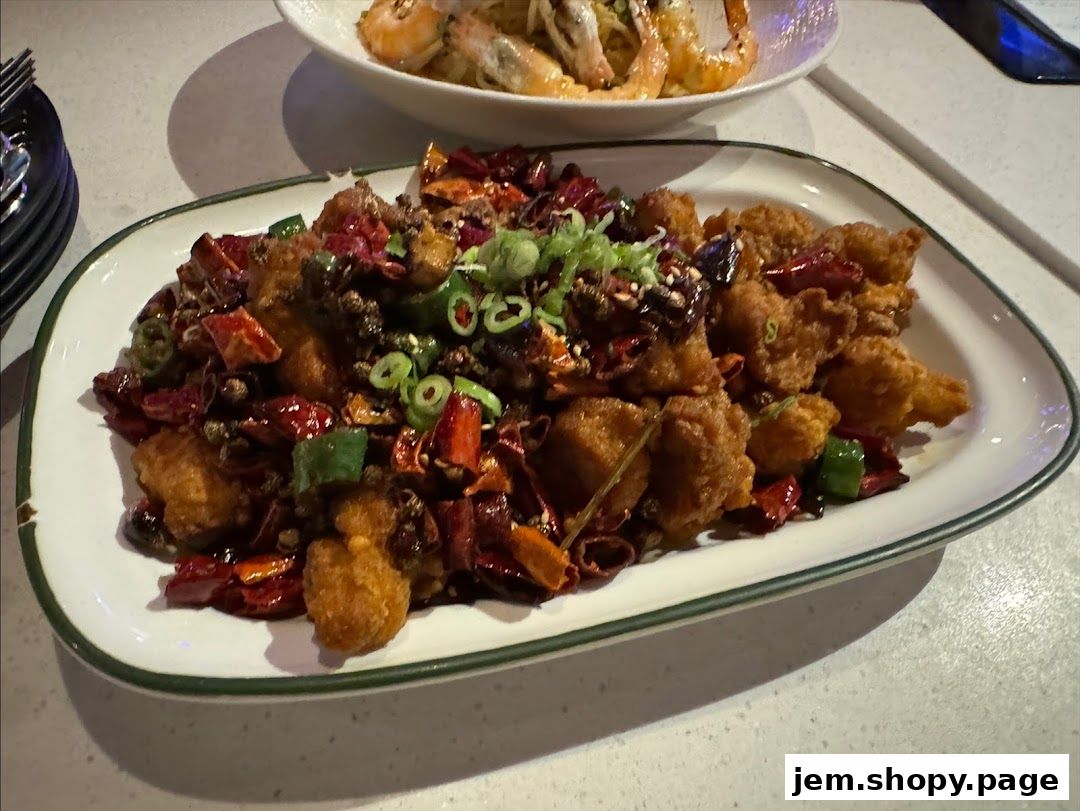 A plate of crispy fried chicken with chili peppers and scallions, served with a side of shrimp pasta.