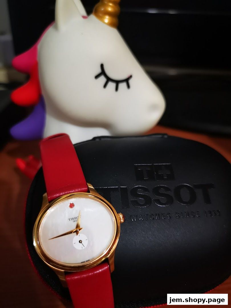 A Tissot watch with a red strap rests on its case next to a unicorn figurine.