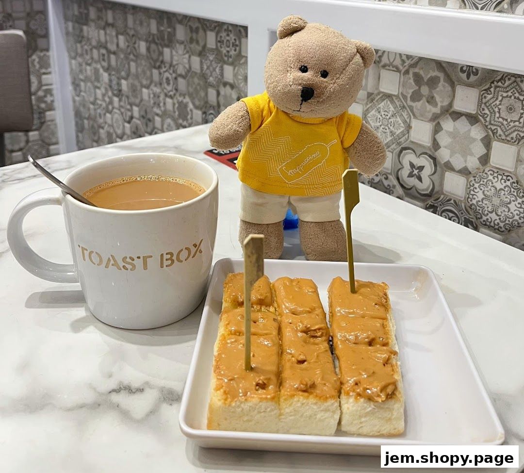 A teddy bear stands beside a mug of coffee and toast with peanut butter.
