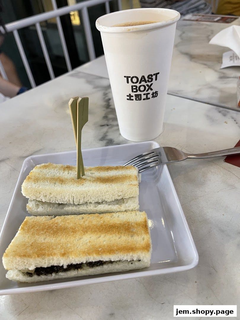 A cup of coffee and two halves of kaya toast on a white plate.