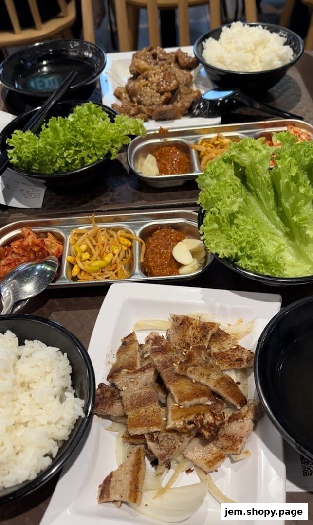 A table laden with Korean dishes, including grilled meats, rice, and fresh lettuce wraps.