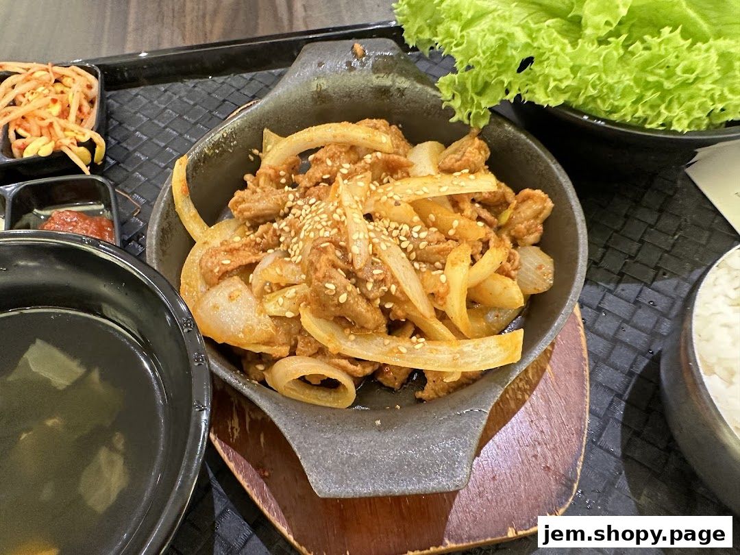 A close-up of a Korean dish with meat, onions, and sesame seeds, served with rice and side dishes.