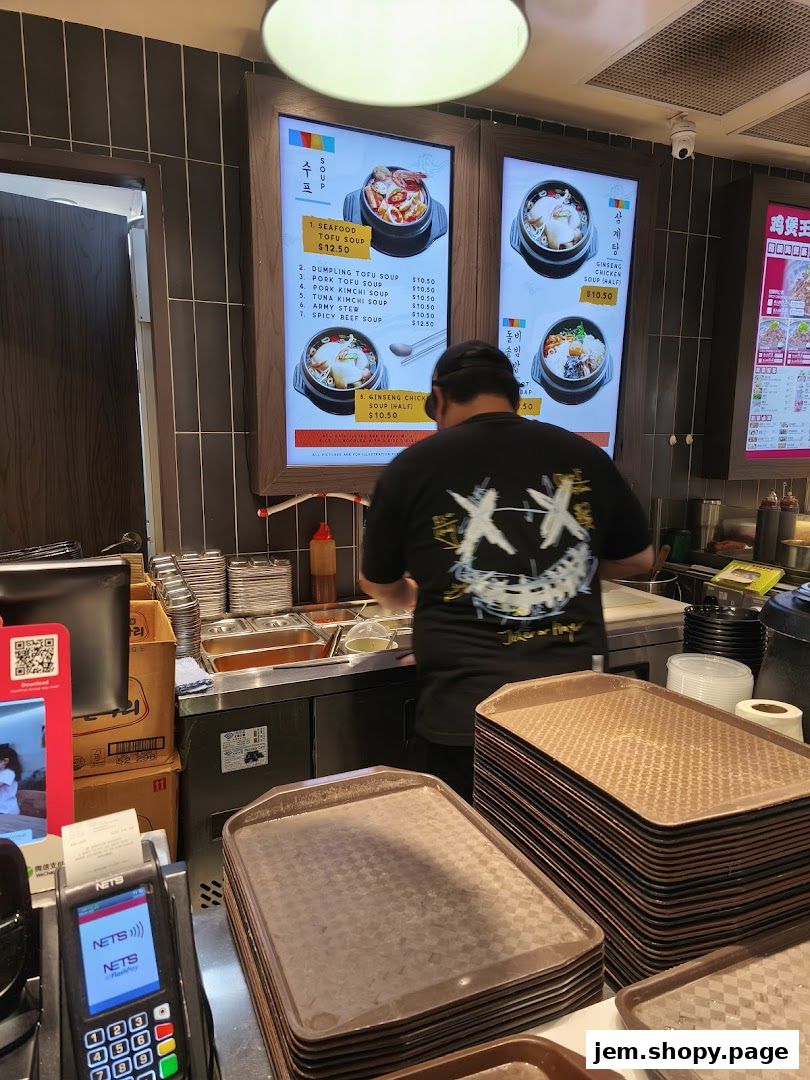 A person stands in front of a digital menu displaying Korean soups at Togi Korean Kitchen.