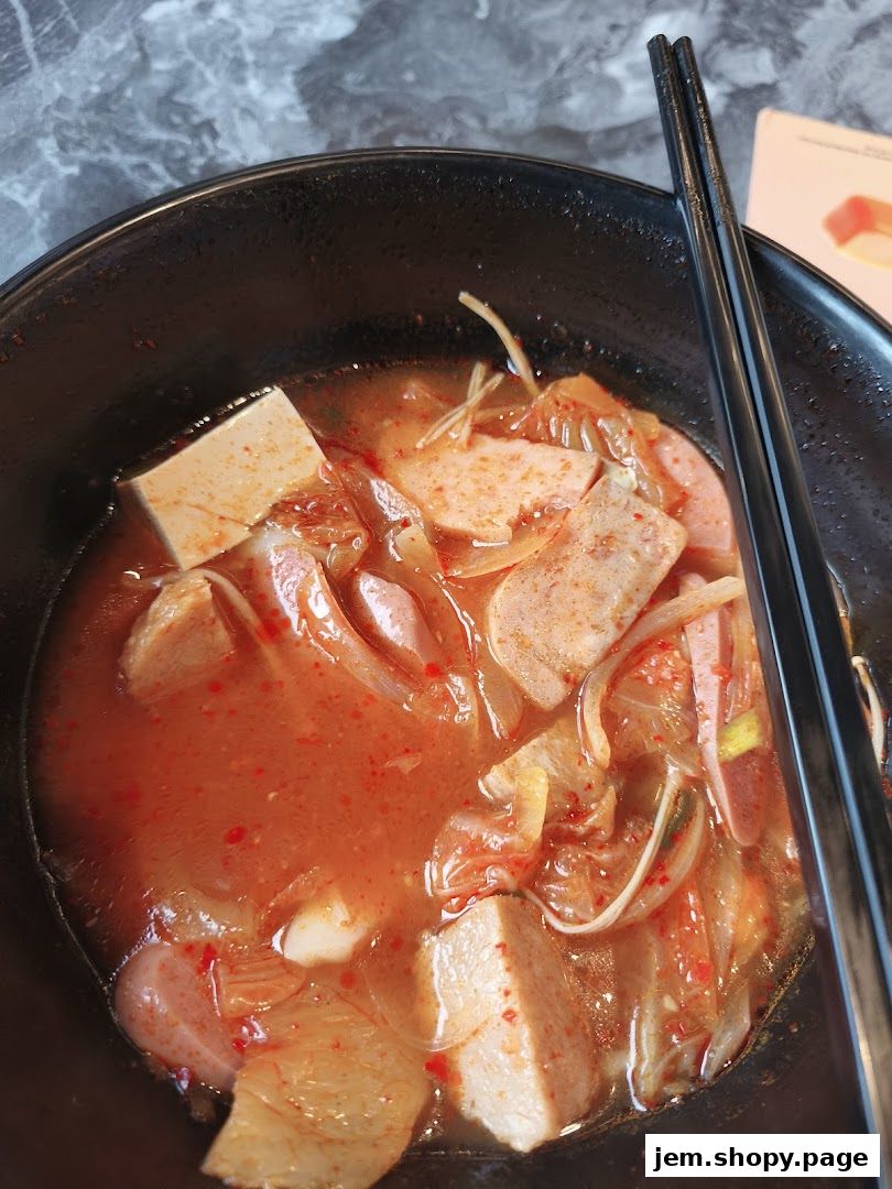 A close-up of a steaming bowl of Korean kimchi stew with tofu and sausage.