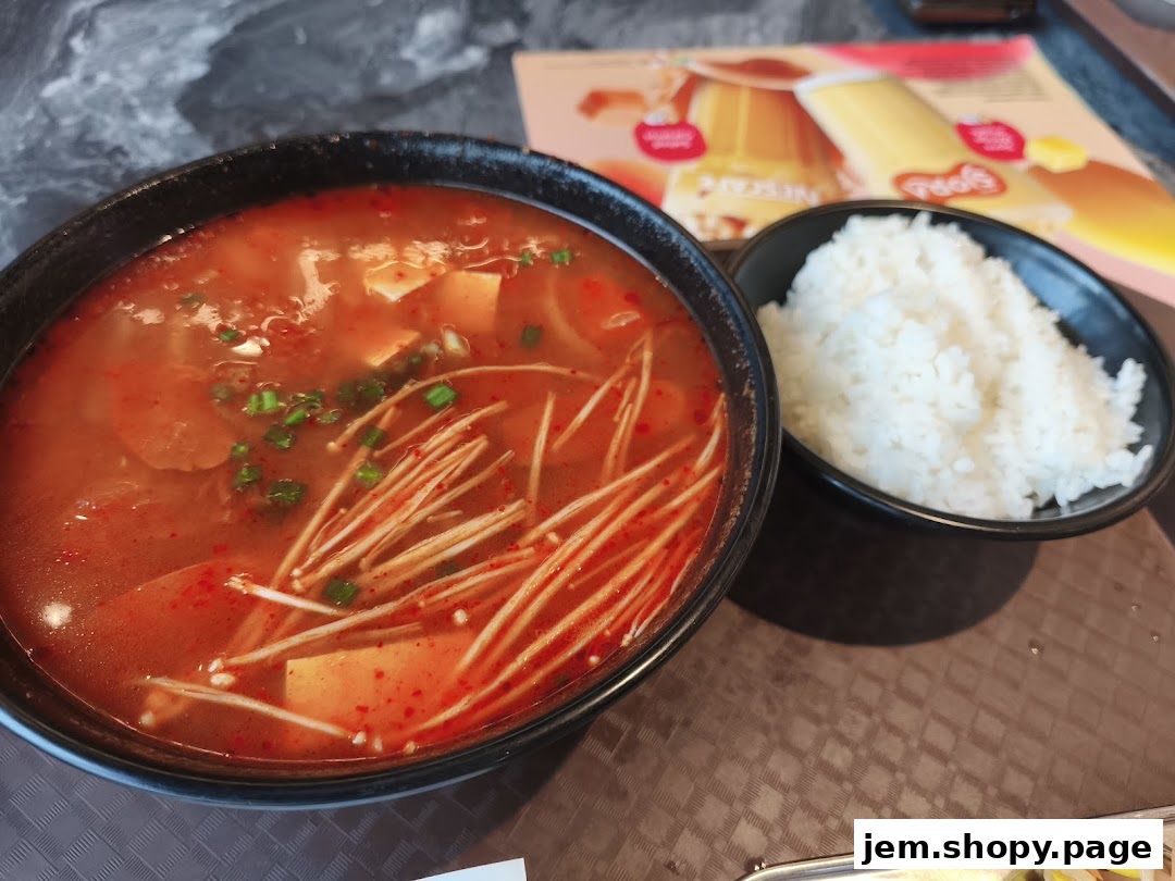 A close-up of a Korean stew with enoki mushrooms and tofu, served with a side of rice.