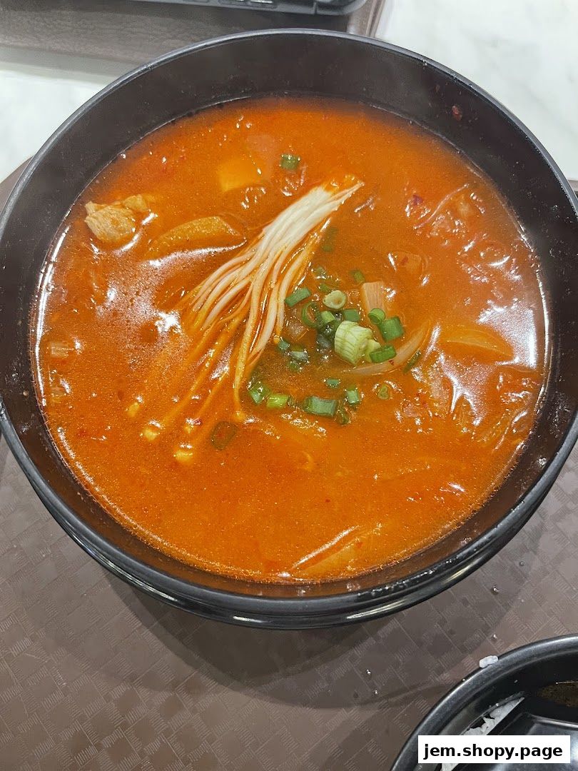 A steaming bowl of Korean kimchi stew with enoki mushrooms and scallions.
