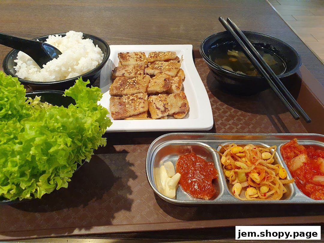 A Korean meal featuring grilled pork belly, rice, kimchi, and soup.