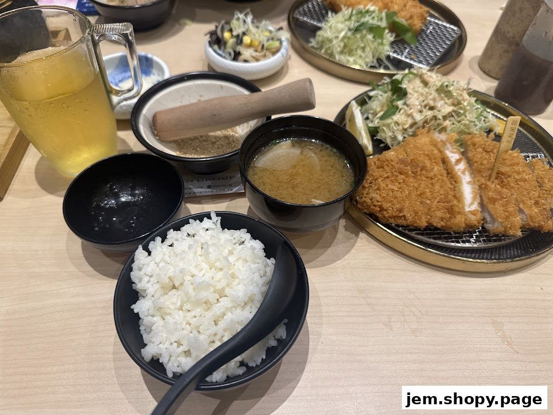 A table setting with tonkatsu, rice, miso soup, and a drink.