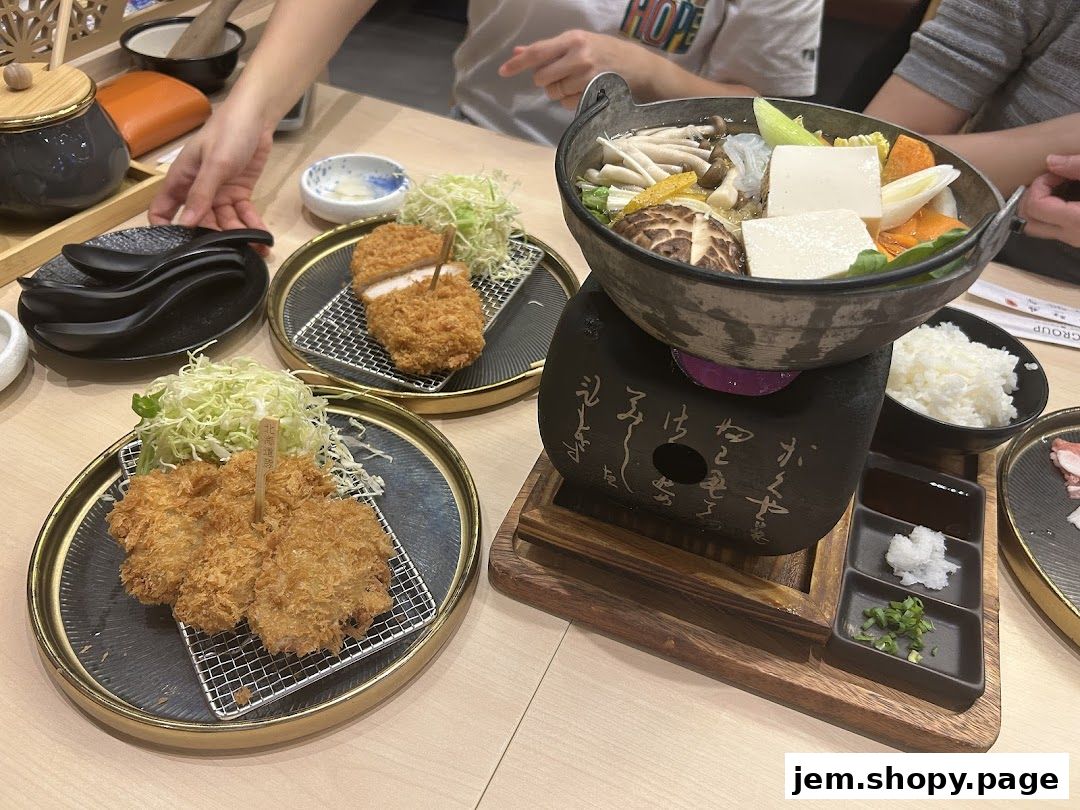 A table setting with two plates of tonkatsu, a hot pot, rice, and dipping sauces.