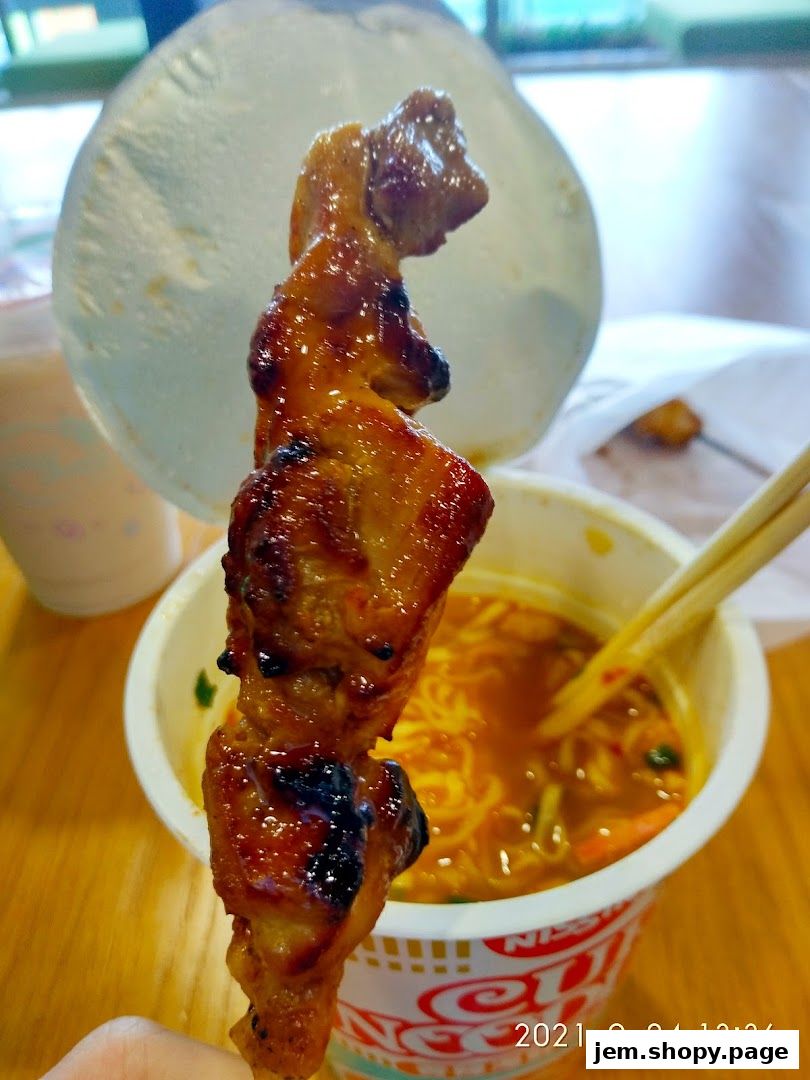 A close-up of a grilled meat skewer held over a bowl of ramen noodles.