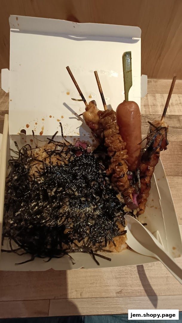 A takeaway box filled with rice, seaweed, and grilled skewers of meat and sausage.