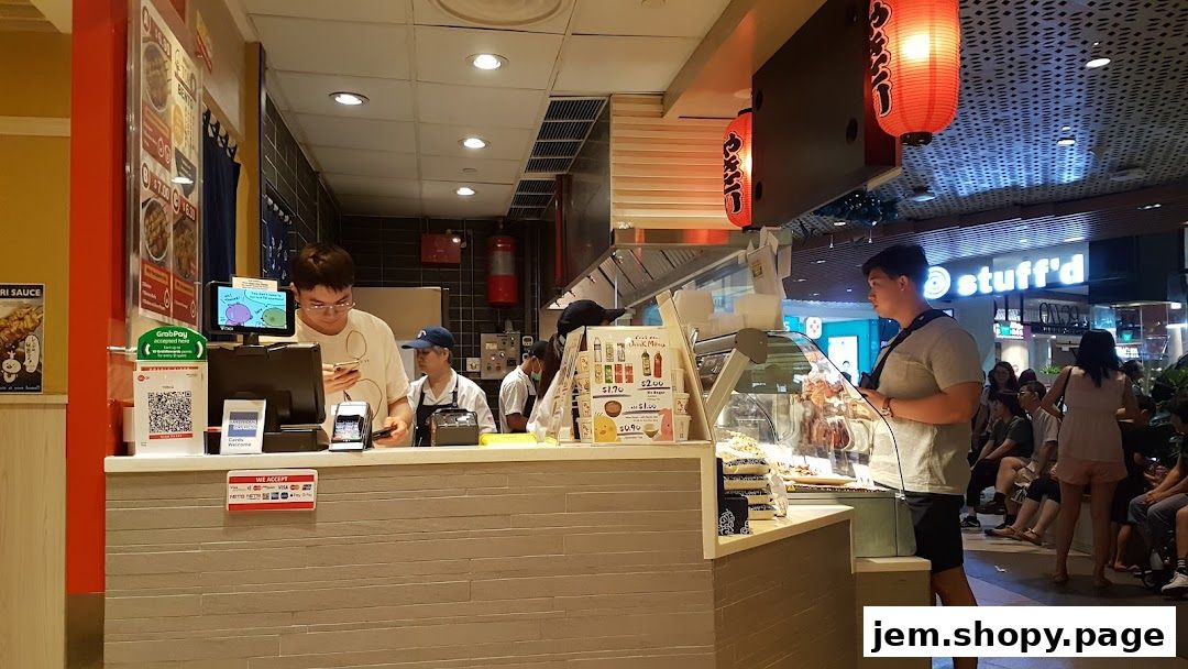 A busy counter at TORI-Q JEM with staff serving customers and a display of food items.