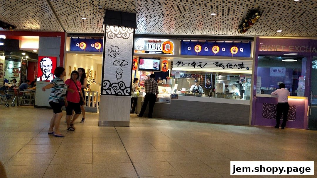 People walking past a TORI-Q food stall and a Swift Exchange counter in a mall.