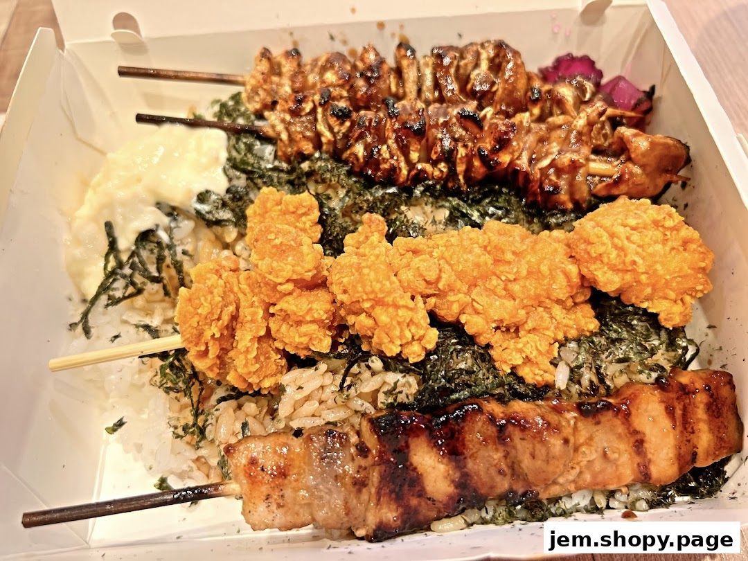 A takeout box filled with rice, seaweed, and various grilled skewers and fried chicken.