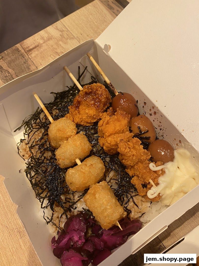 A bento box filled with rice, seaweed, fried chicken, and other skewers.