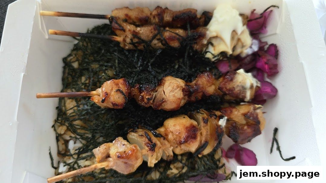 A bento box filled with rice, seaweed, and grilled chicken skewers.