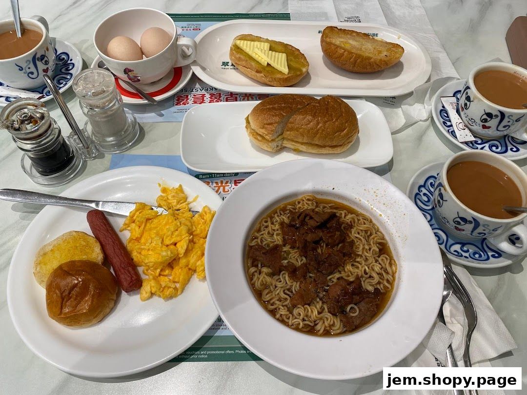 A table laden with a hearty breakfast spread including noodles, eggs, sausage, toast, and milk tea.