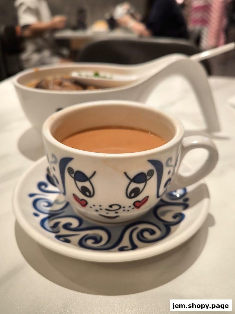 A close-up of a decorative teacup filled with milk tea, with a bowl of food in the background.