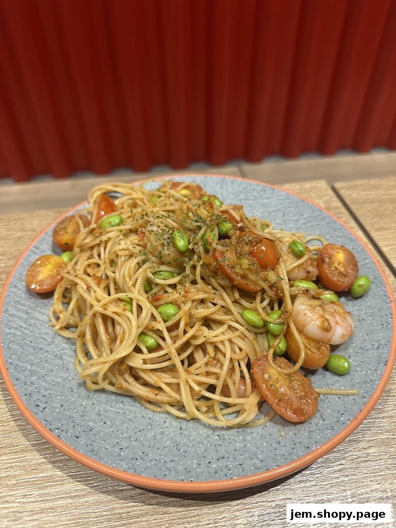A plate of spaghetti with shrimp, cherry tomatoes, and edamame beans.